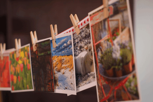 A series of colourful postcards hung on a washing line with small wooden pegs.